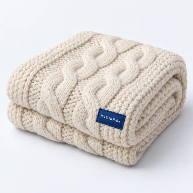 Folded cream cable-knit blanket with a cobalt Idle Hours fabric label