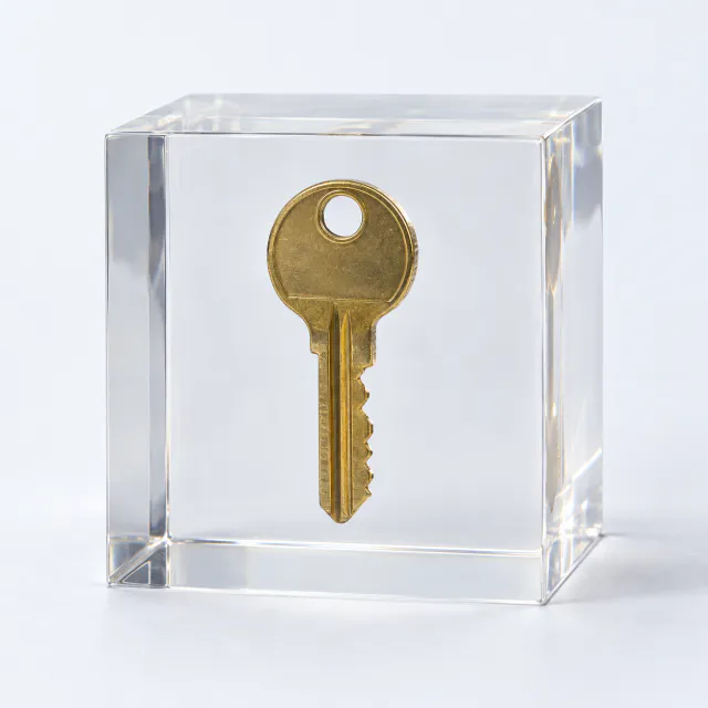 Clear acrylic cube with a brass key suspended inside on a pale gray background